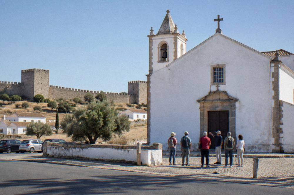 A small group listening to a guide outside a whitewashed church in the Alentejo countryside