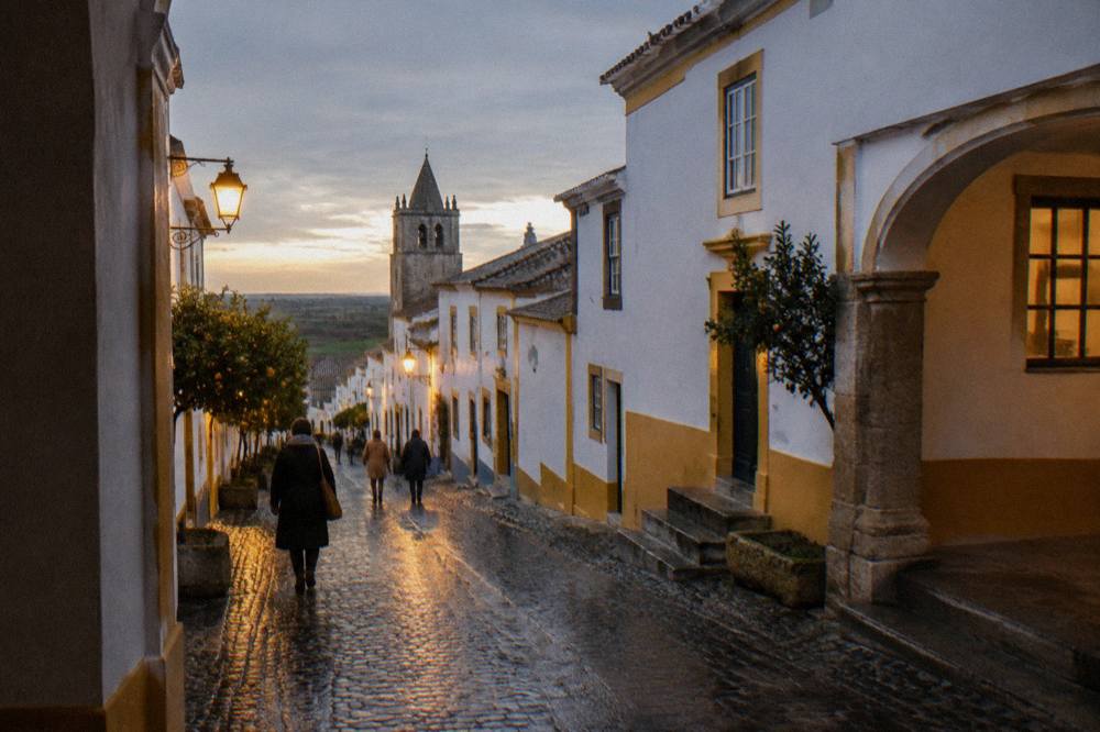 A cobbled street in Évora with wet stones reflecting lantern light on a cold December evening