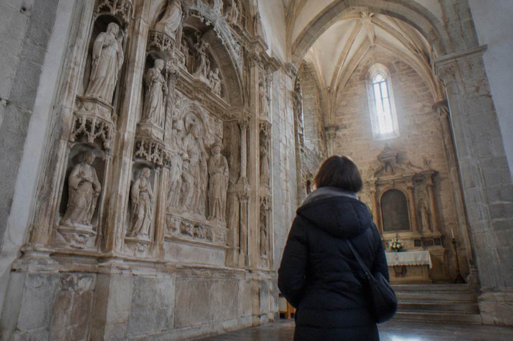 A visitor in a winter coat looking at the carved stone interior of a chapel in Évora