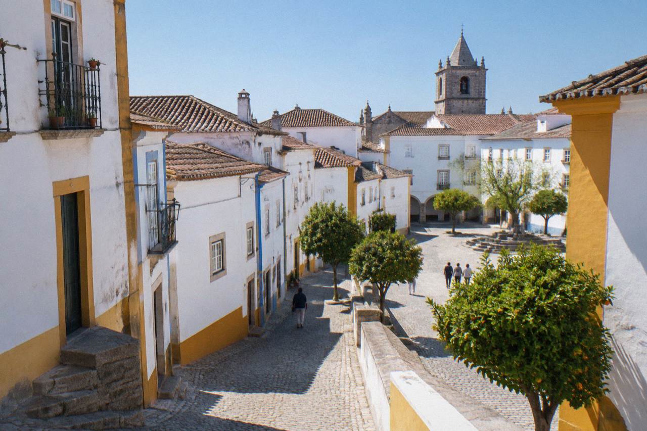 Sunlit square in the historic centre of Évora with white buildings and a church tower