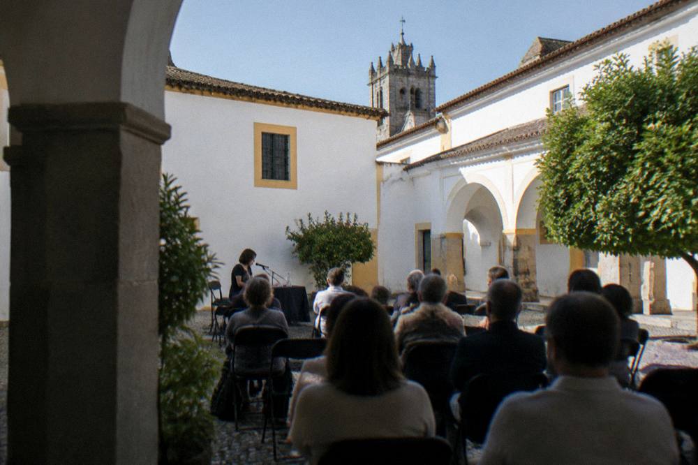 Author speaking at an outdoor literary event with rows of seated listeners in a Évora courtyard