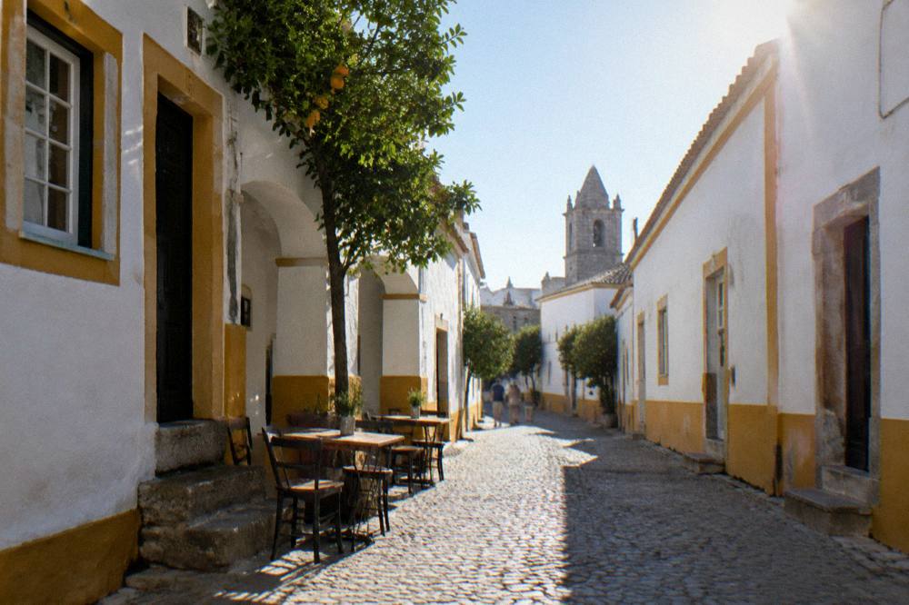 A narrow old-town street in Évora with small tables outside a tavern door