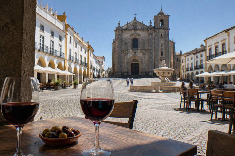 Glasses of red Alentejo wine on a wooden tasting table beside a plate of olives