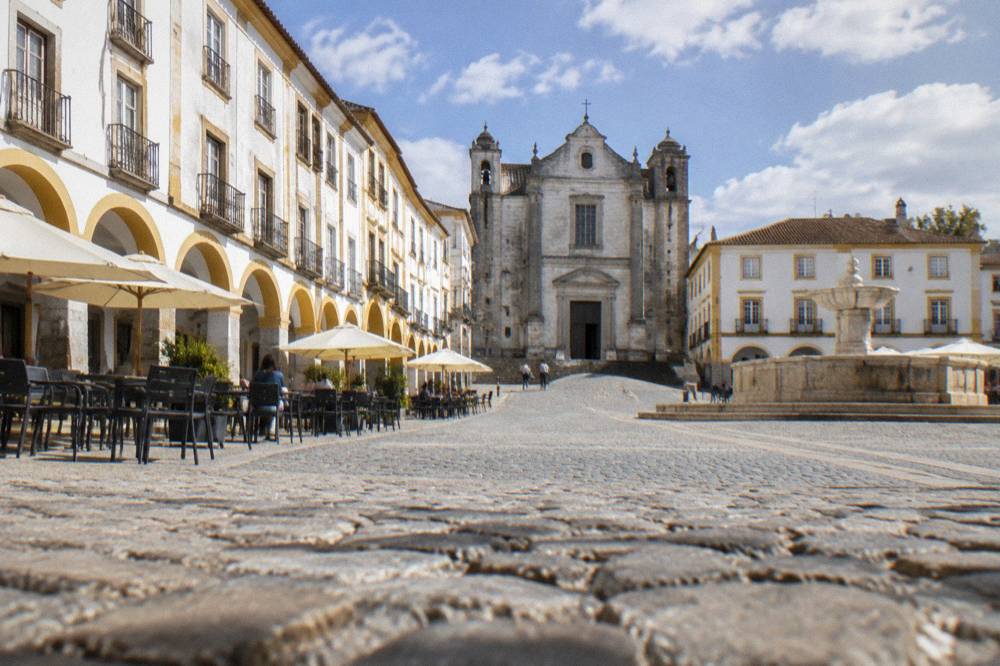 The arcade of Praça do Giraldo with café tables and the fountain in Évora