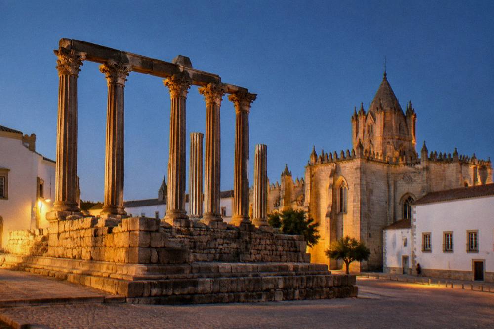 The Roman temple of Évora lit by evening sun with the cathedral beyond