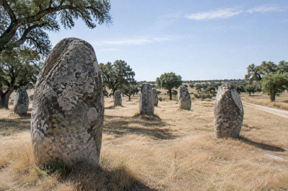 A stone circle of standing menhirs on open grassland under a wide sky