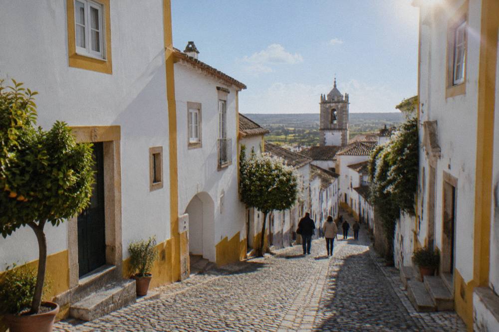 Cobbled street in the historic centre of Évora lined with whitewashed houses and yellow trim under a spring sky