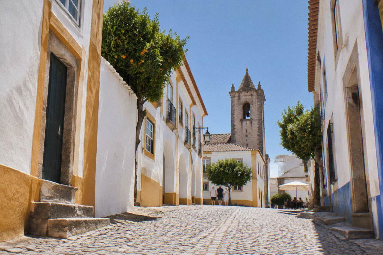 Sunlit square in Évora with white houses and a church tower under a deep blue summer sky
