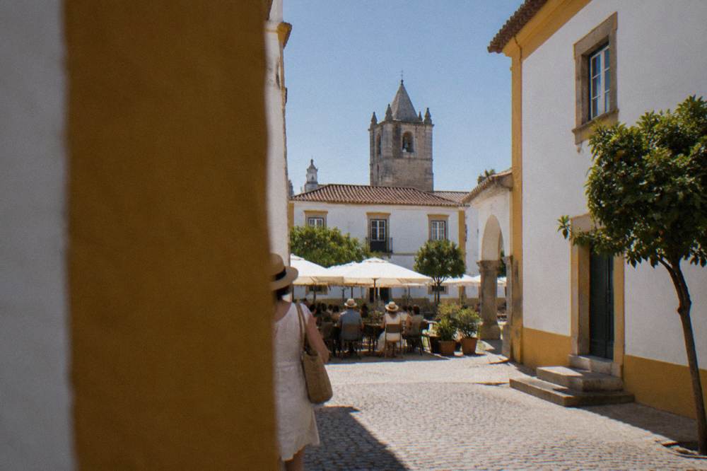 People dining at outdoor tables on a warmly lit Évora square in the evening