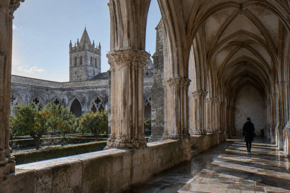The Gothic cloister of Évora's cathedral in low winter light, with a single visitor walking the arcade