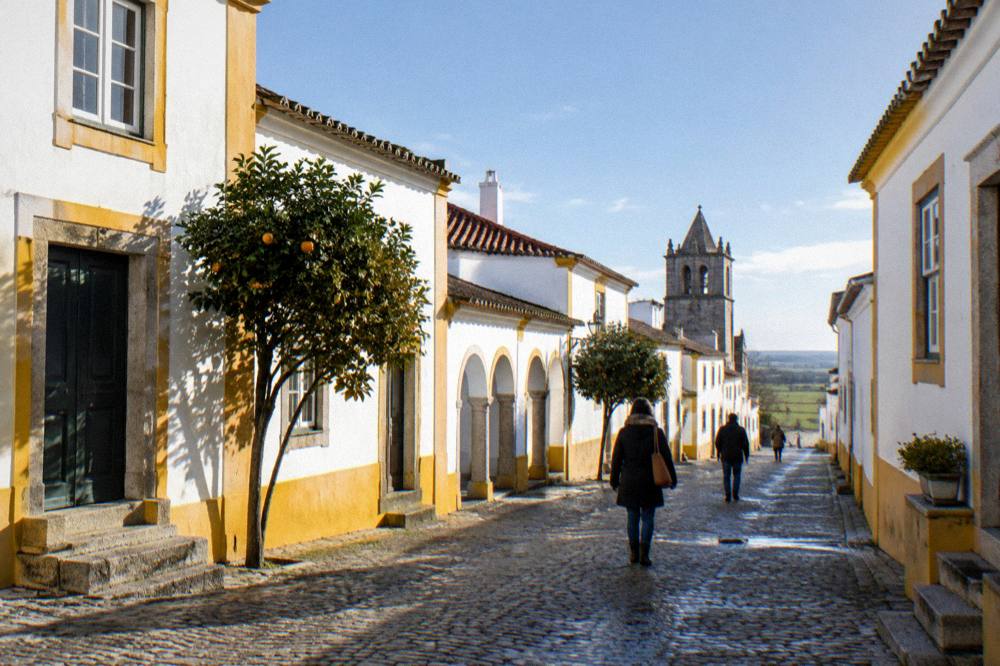 A quiet lane of whitewashed houses with yellow trim inside Évora's walls on a mild winter afternoon
