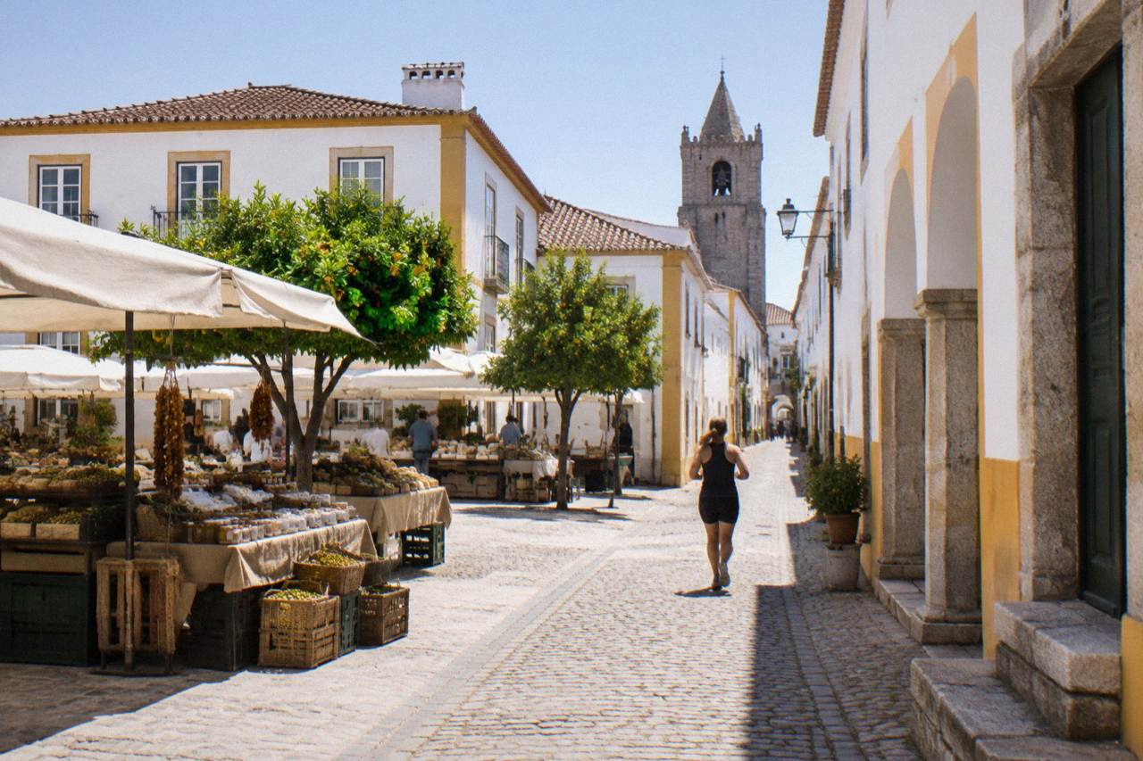 Market stalls with regional goods set out under awnings in a sunlit square in Évora