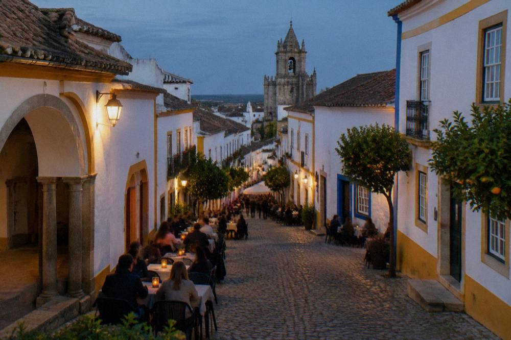 People dining at outdoor tables on a cobbled street in Évora in the evening