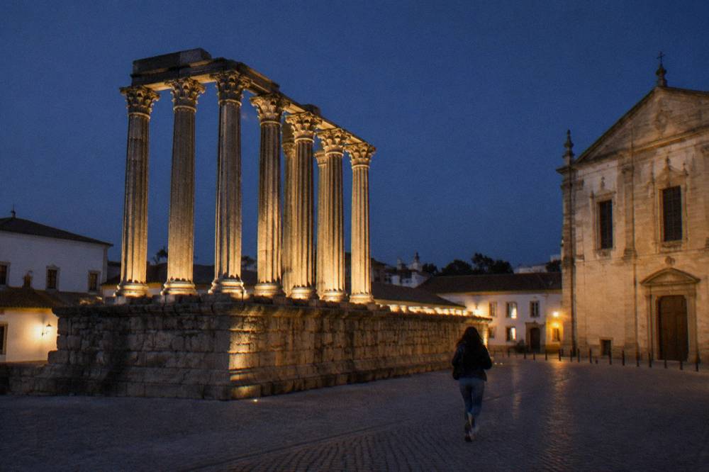 The floodlit Roman temple columns in Évora seen at night with a dark sky behind them