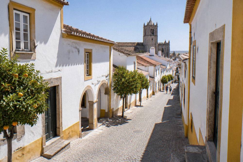Harsh midday sunlight cutting deep shadows across a whitewashed street in Évora