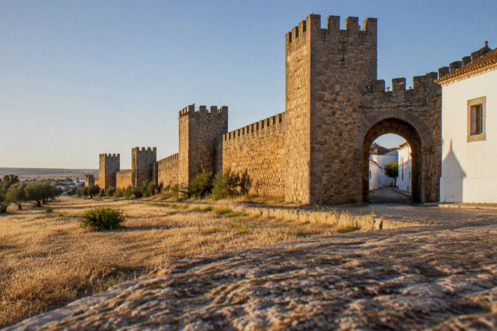 Sunset light striking the medieval walls and towers of Évora from open ground outside the city