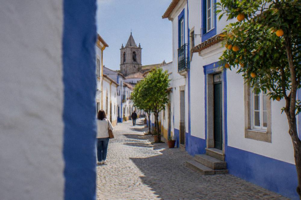 Sunlit narrow street in Évora with whitewashed walls and blue trim
