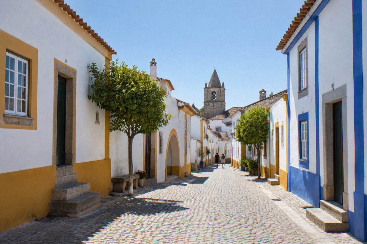A quiet cobbled street inside the walled historic centre of Évora with whitewashed houses and blue and yellow trim