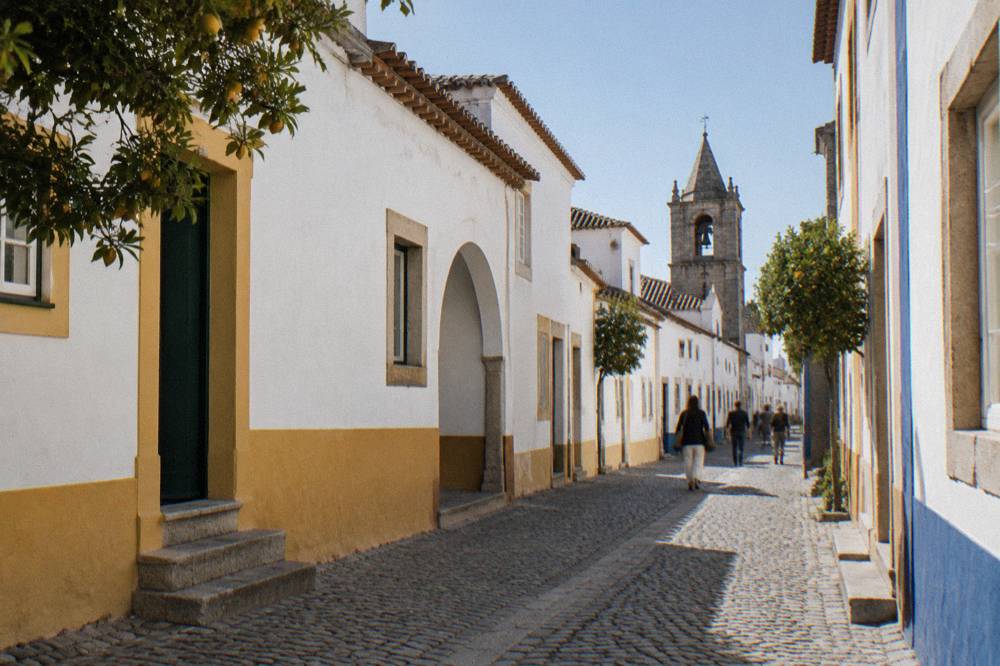 Visitors walking along a narrow cobbled lane in Évora lined with whitewashed buildings