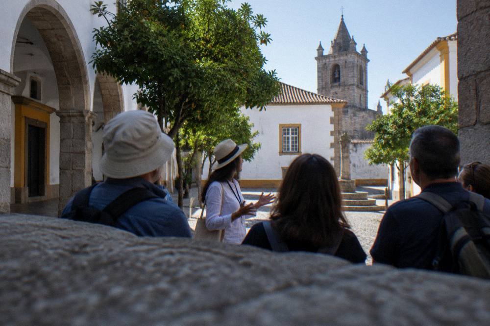 A guide speaking to a small group of visitors in a shaded square in Évora