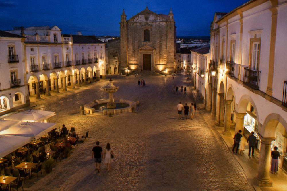 The tourist office arcade on the Praça do Giraldo in Évora with visitors reading a map at dusk