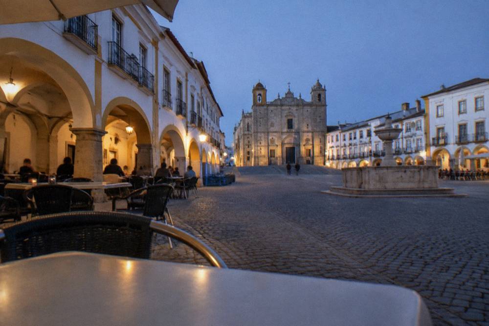 The arcaded Praça do Giraldo in Évora at dusk with café tables under the arches