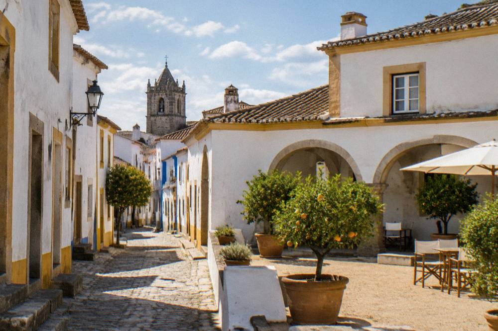 Sunlit hotel courtyard in Évora with whitewashed walls and potted orange trees