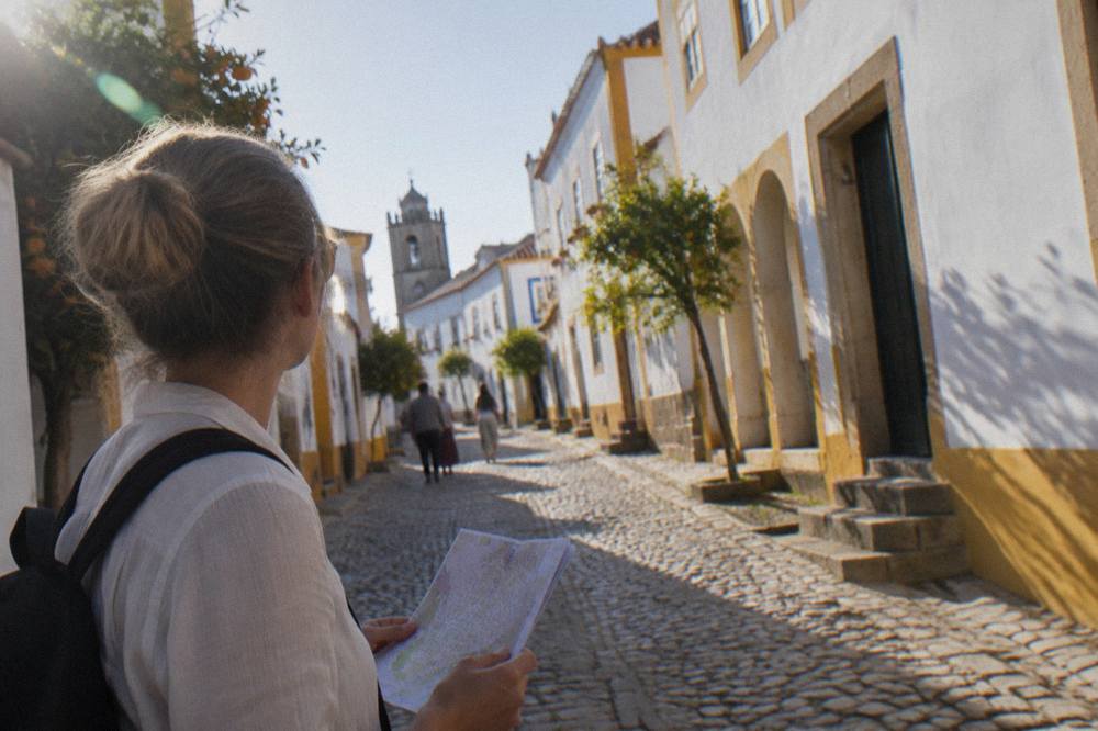 Visitor holding a paper city pass while standing on a cobbled street of white-washed houses in Évora
