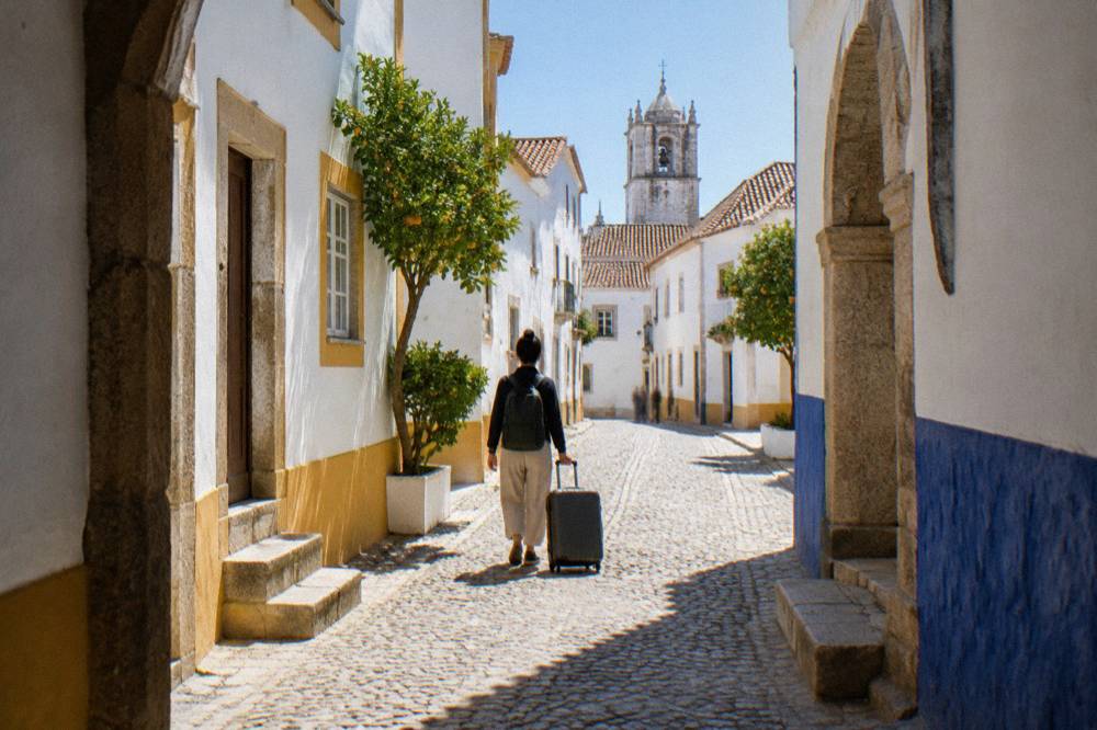 A traveller with a suitcase walking through a sunlit Alentejo street towards the station