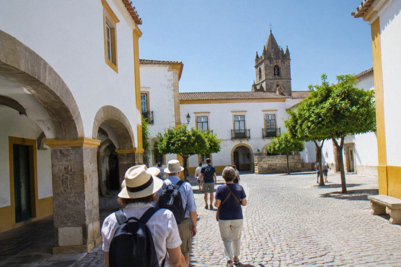 Guide leading a small group of visitors through a sunlit cobbled square in the walled centre of Évora