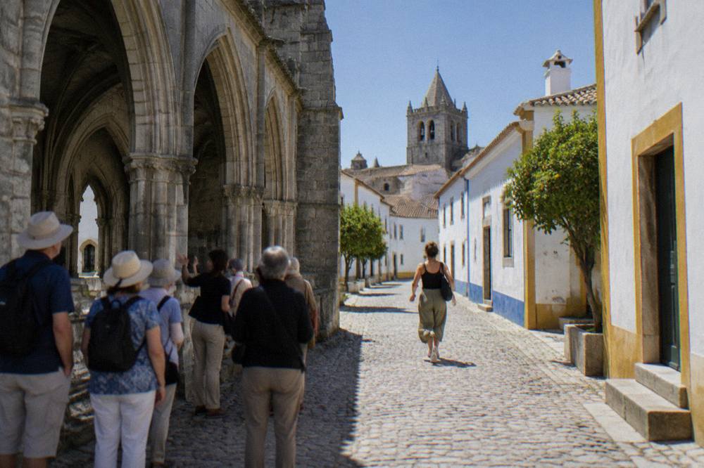 Visitors listening to a guide beside the granite arches of Évora's Gothic cathedral cloister