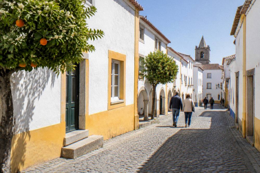 Visitors in light jackets walking a cobbled Évora street under spring sunshine