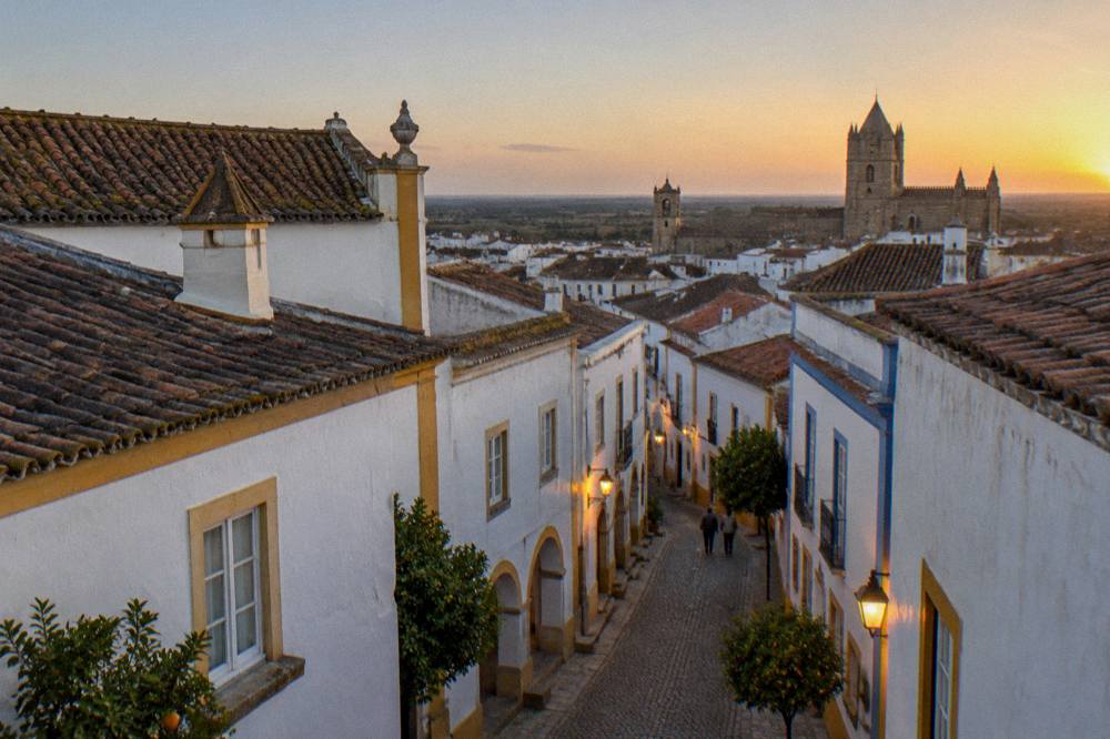 Golden evening light over the tiled rooftops and church towers of Évora seen from a rooftop terrace