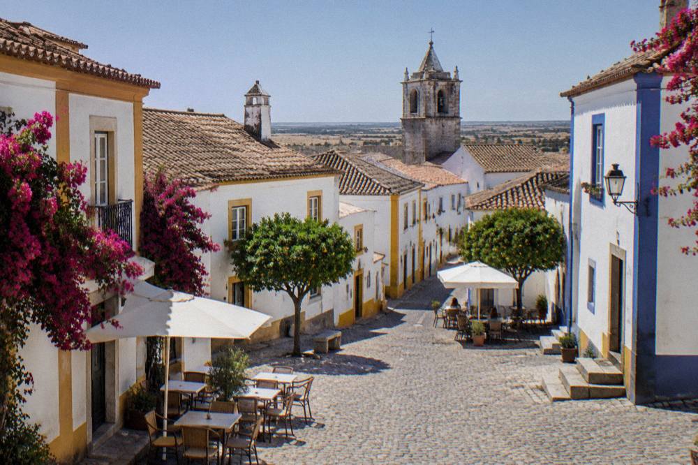 A quiet cobbled square in Évora with white houses, bougainvillea and outdoor cafe tables
