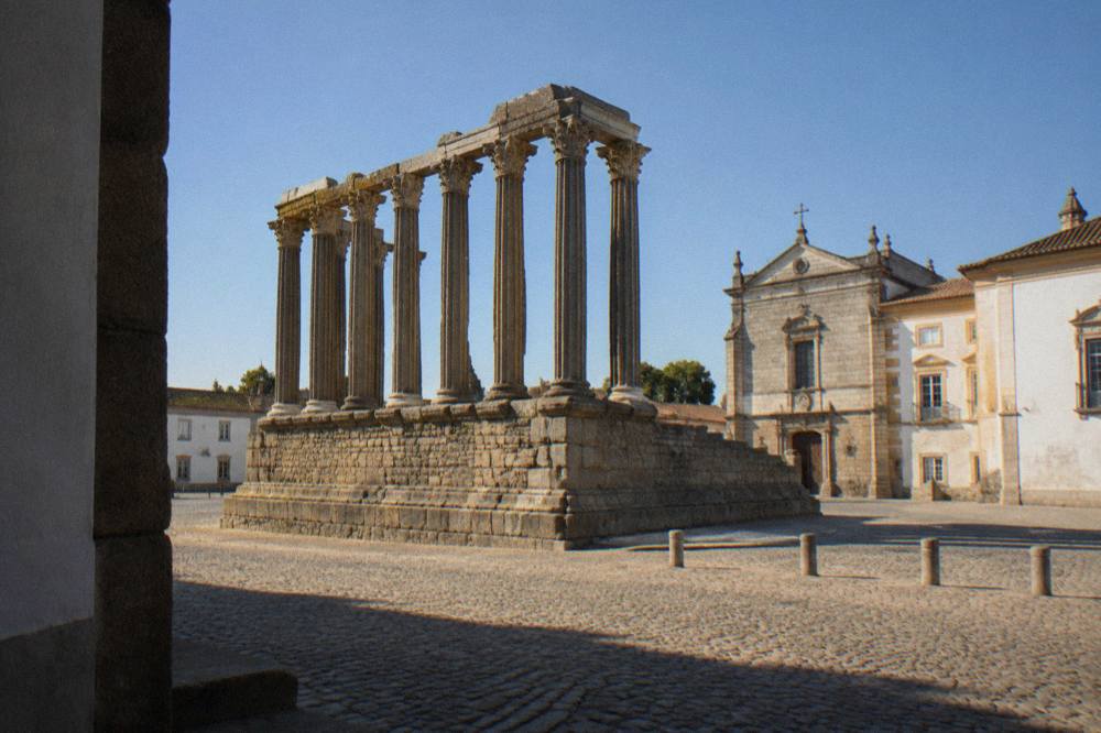 The Roman temple columns of the Templo Romano in Évora rising above a cobbled square at golden hour