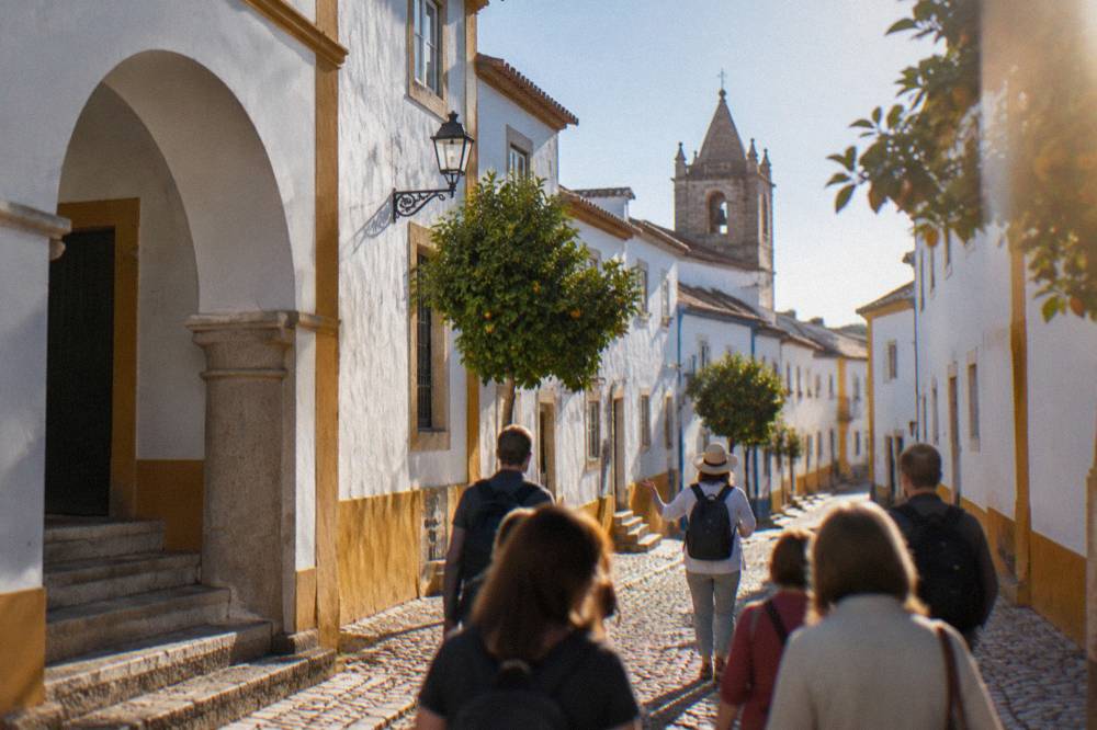 A guide leading a small group of visitors along a narrow golden stone street in Évora
