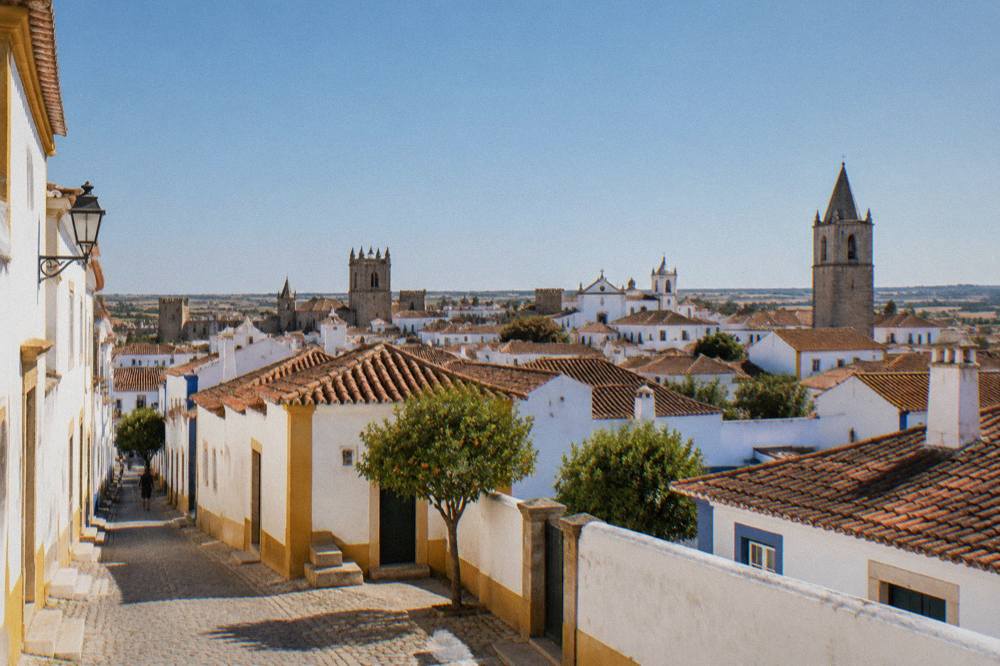 A wide view over rooftops and church towers inside the walls of Évora at golden hour