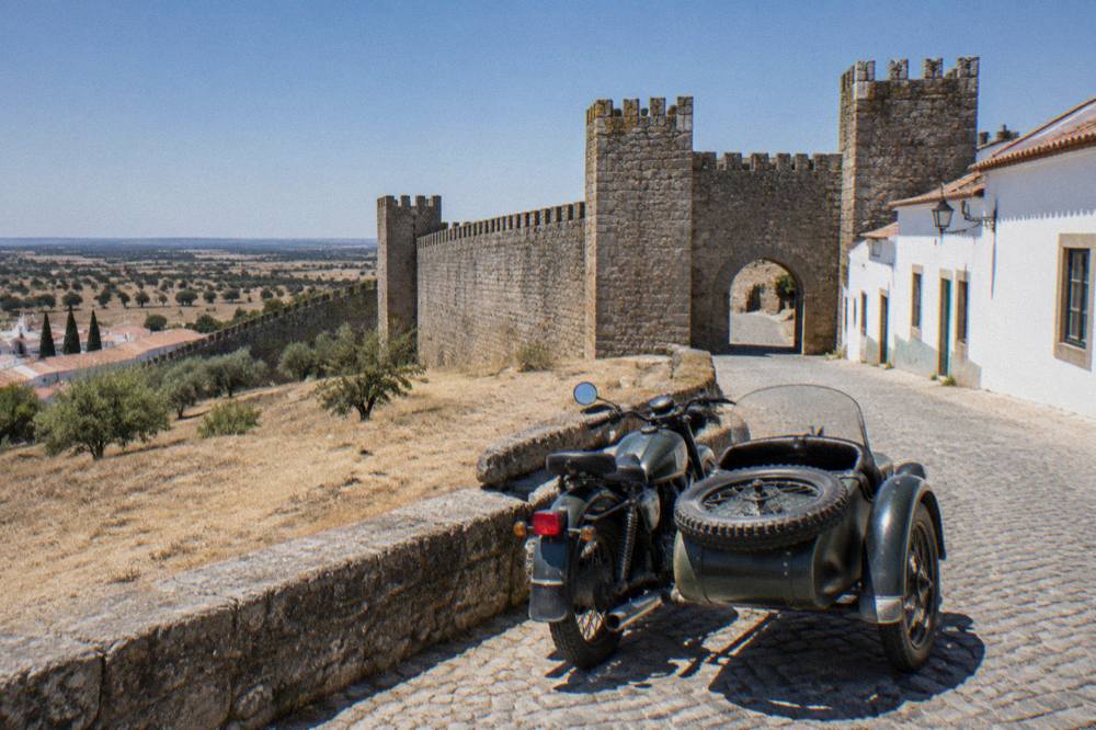 A vintage motorcycle sidecar parked on a cobbled street beside Évora's city walls