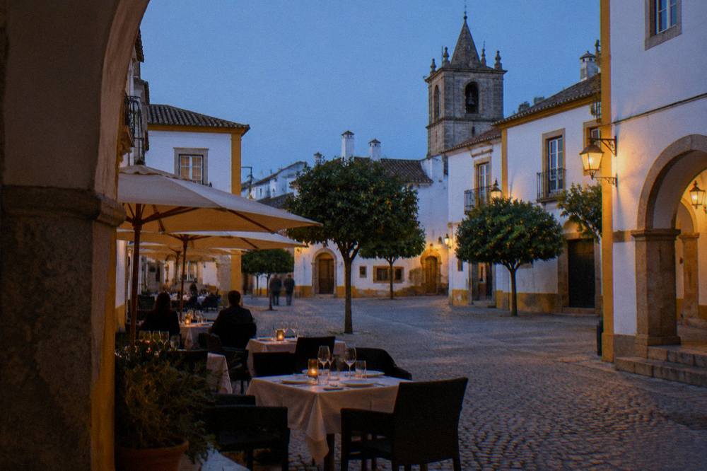 A restaurant terrace with tables set for dinner on a warm evening in a Portuguese square