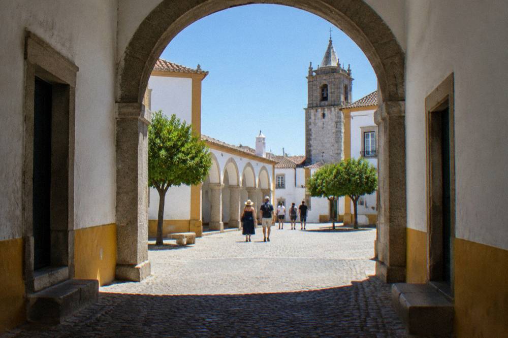 Visitors walking through a stone archway into a small square in Évora