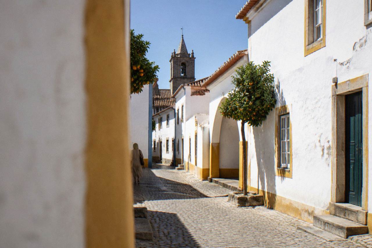 Sunlit whitewashed houses and a church tower in Évora under a clear blue sky