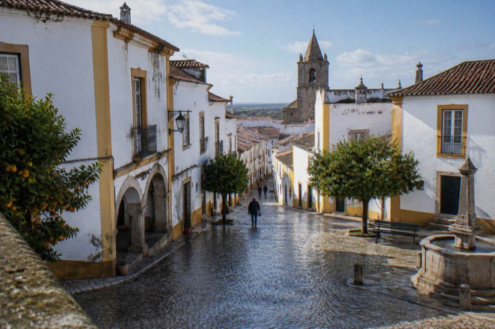 Rain-darkened cobbled square in Évora with reflections on the stones
