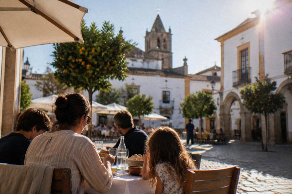 A family sharing a long lunch at an outdoor table in a square in Évora