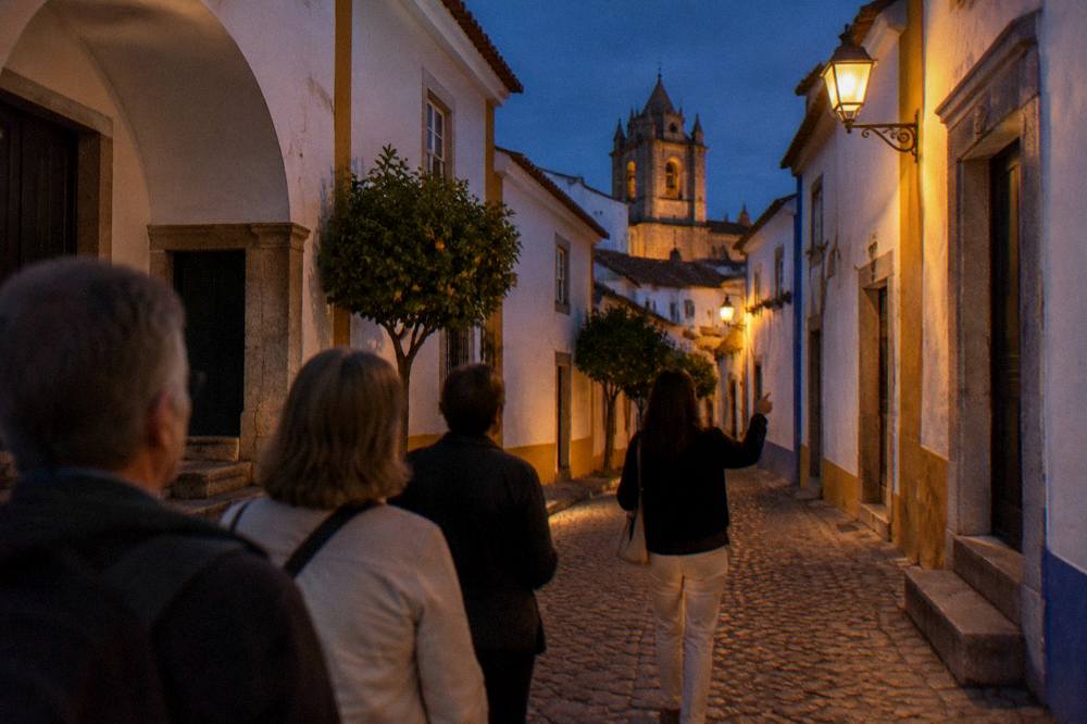 A guide leading a small group of visitors along a narrow cobbled street in Évora at dusk