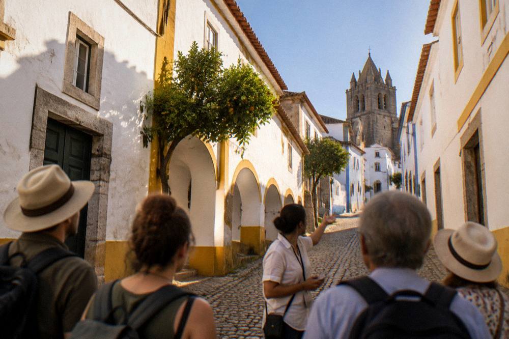 A guide speaking to a small group of visitors on a cobbled street of white houses in Évora