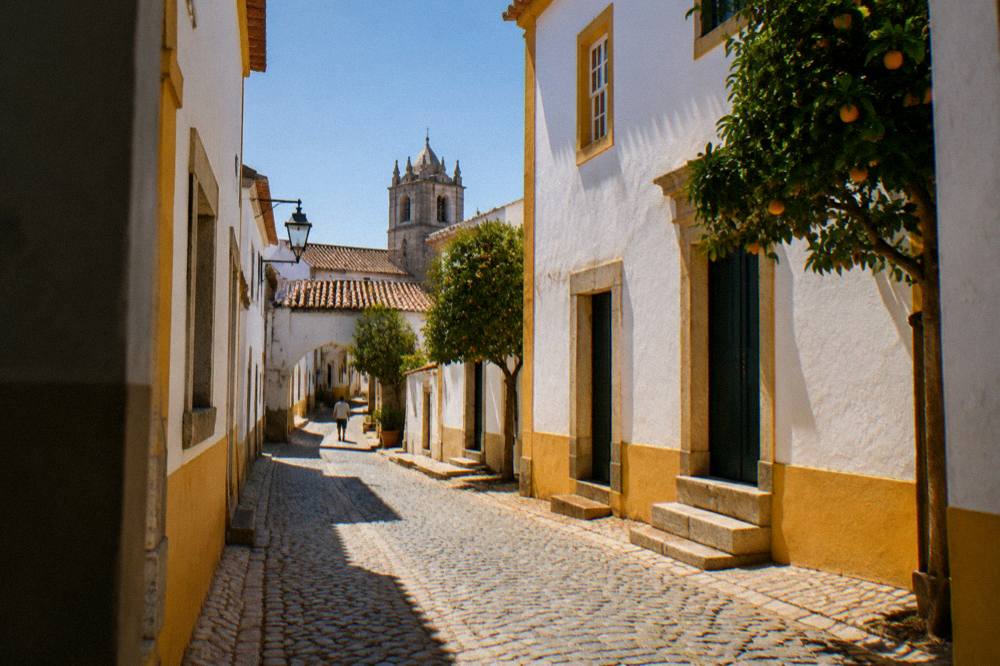 A narrow cobbled street of white houses with yellow trim and blue sky in the historic centre of Évora