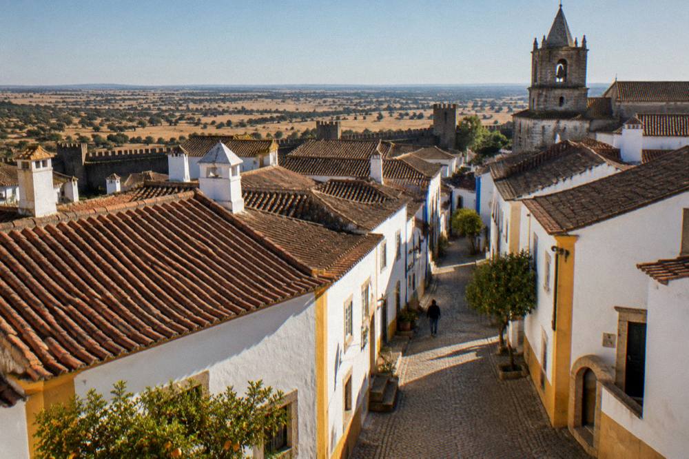 View over the rooftops and walls of Évora toward the Alentejo plain at sunset