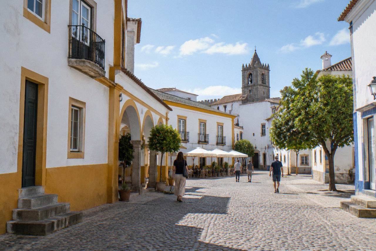 Sunlit square in the historic centre of Évora with white walls and people walking calmly