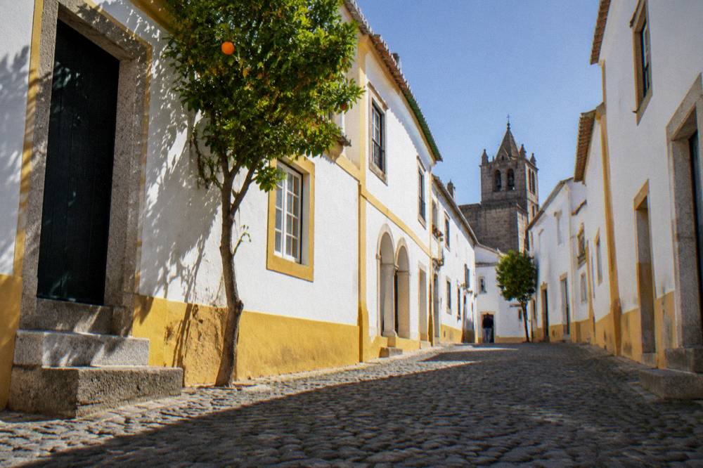 A sunlit street of white houses with yellow trim inside the walls of Évora