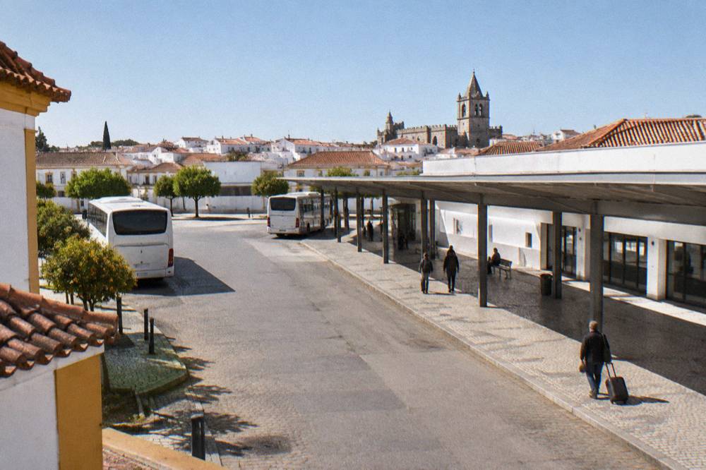 A city bus and coach terminal building with a covered platform area and a few travellers
